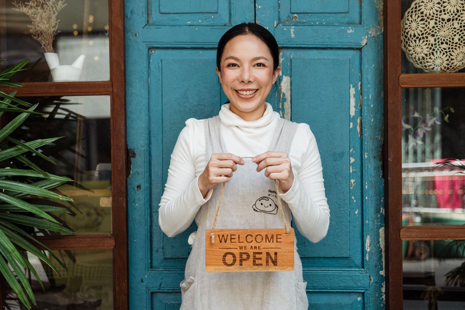 Small business owner holding an OPEN sign, ready to pay her team